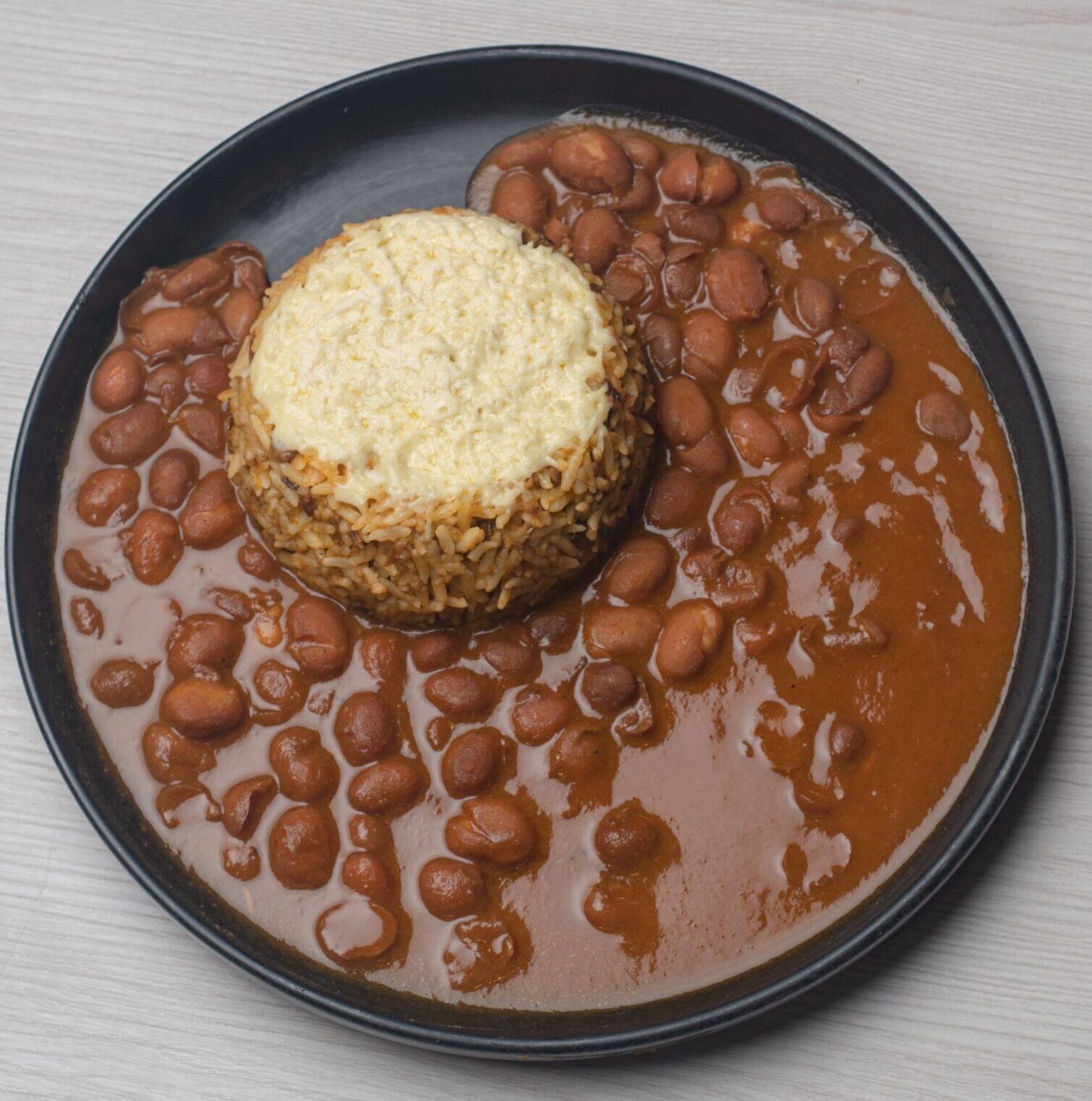 Aerial shot of a rice and bean dish with rich sauce on a black plate, perfect for cooking blogs.
